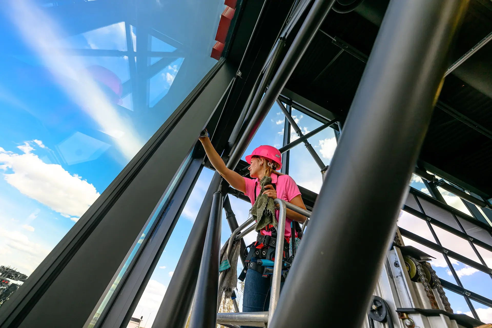 Linnae cleaning commercial glass from a lift in a pink hard hat - Peace Home Services Grande Prairie