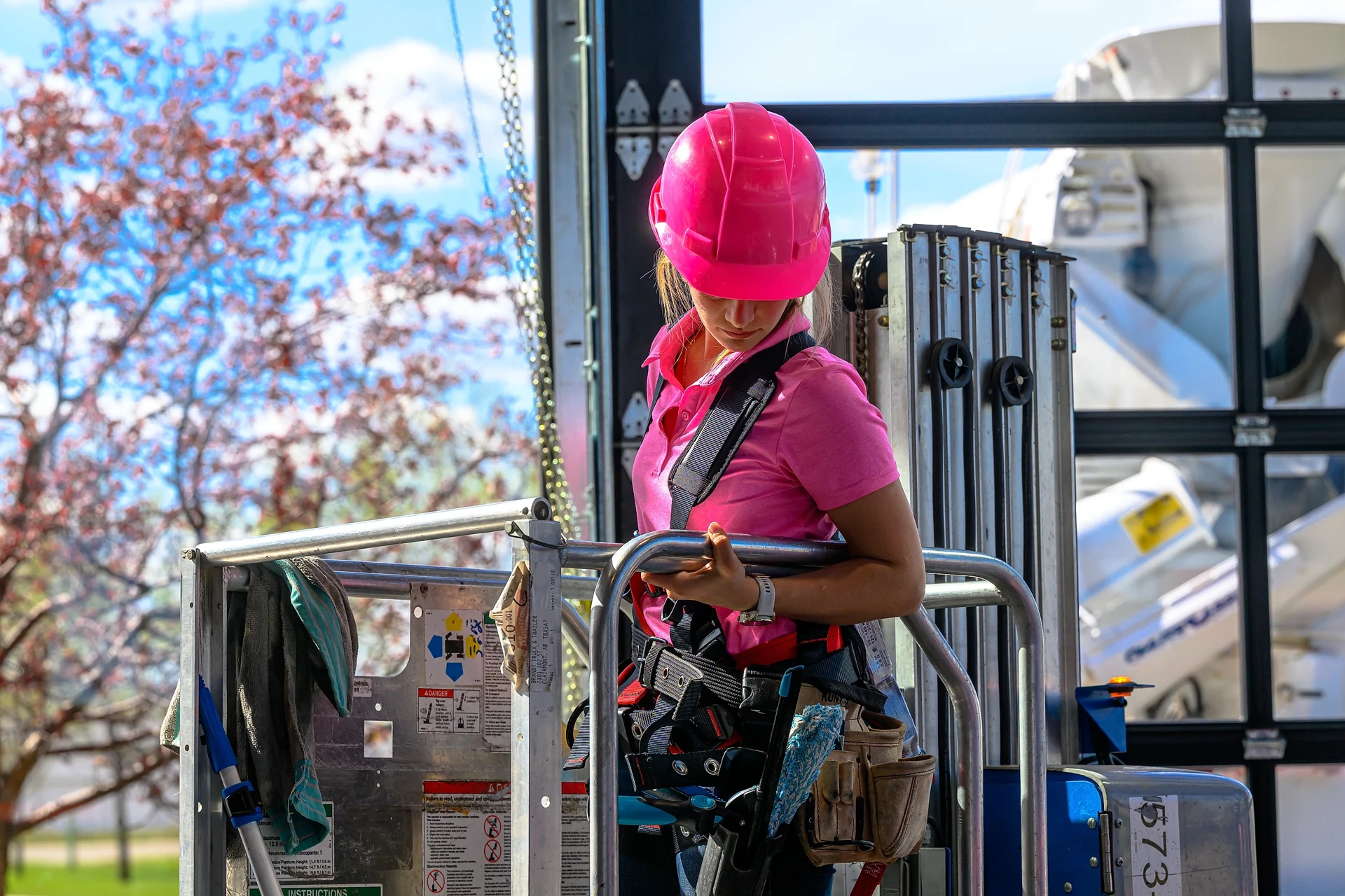 Linnae Biegel, Owner of Peace Home Services, in a pink hard hat on a lift cleaning commercial glass
