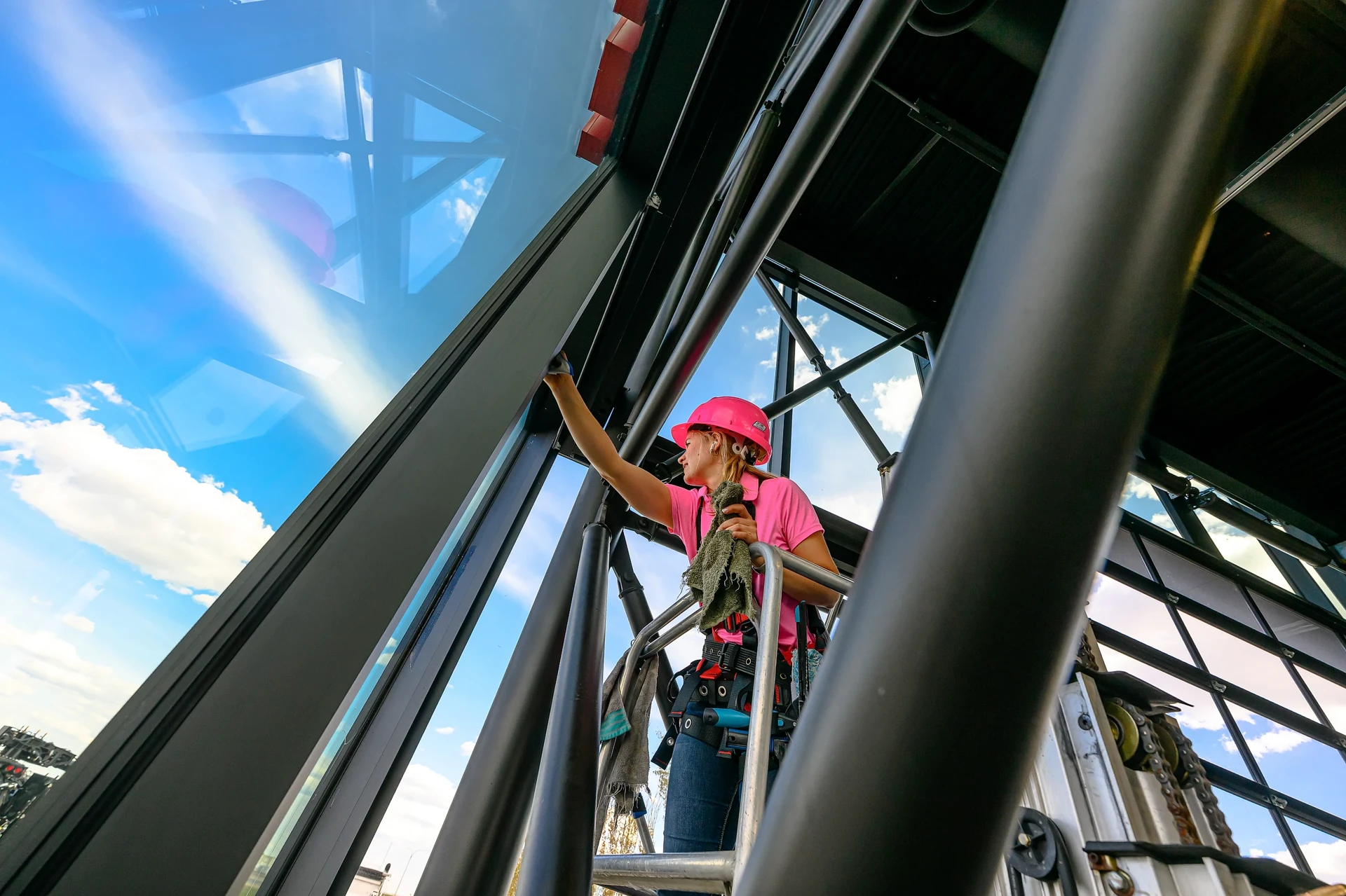 Linnae cleaning commercial glass from a lift in a pink hard hat - Peace Home Services Grande Prairie